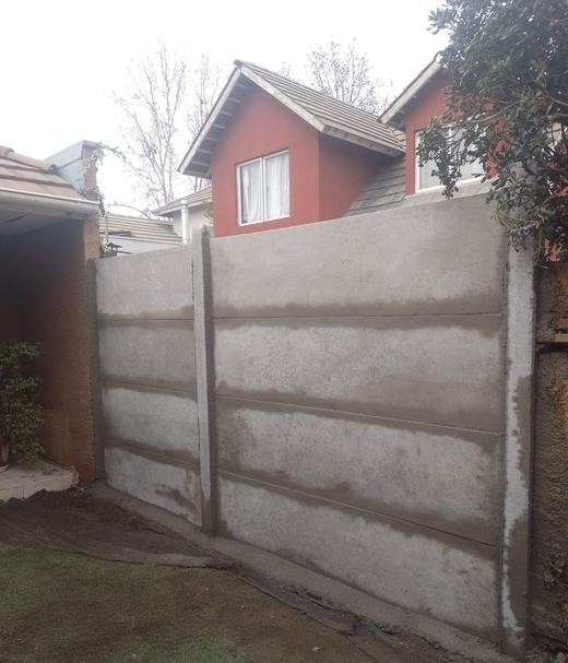 Cierre de concreto vibrado junto a una vivienda con techo rojo.