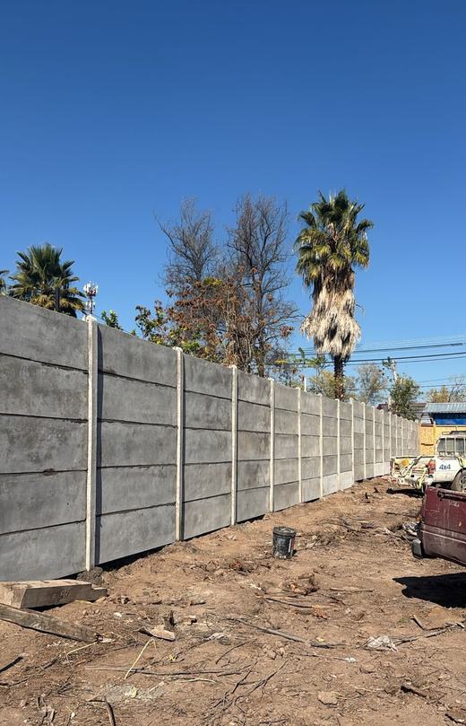 Cierre perimetral de concreto vibrado con palmeras y cielo despejado al fondo.