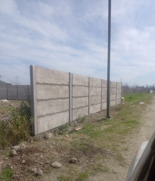 Cierre perimetral de concreto vibrado junto a un camino de tierra.
