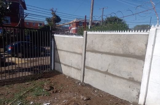 Cierre perimetral de concreto vibrado junto a una vivienda, al atardecer.