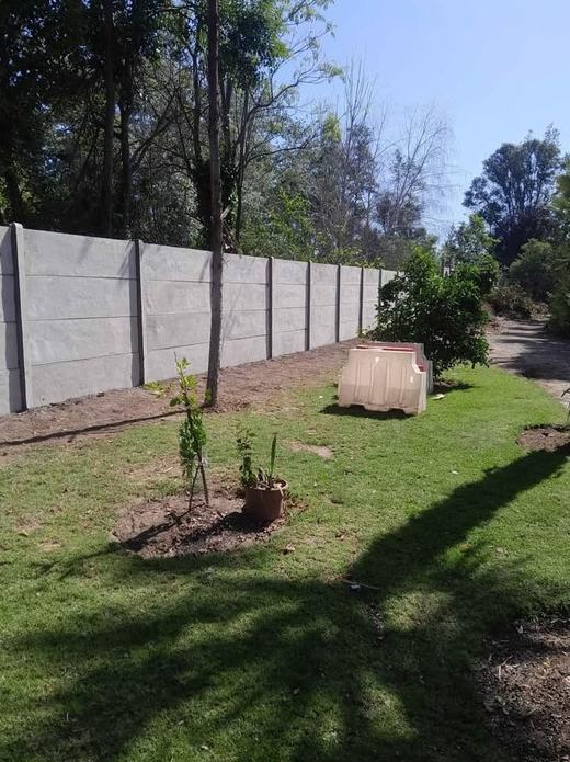 Cierre perimetral de concreto vibrado en un jardín con árboles.