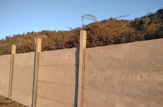 Cierre perimetral con postes de madera y paneles de concreto.