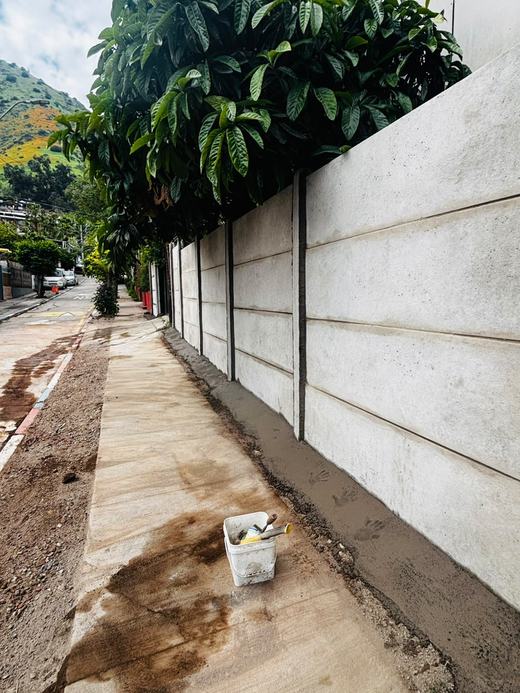 Cierre perimetral de concreto vibrado en una vereda, con un balde de pintura.